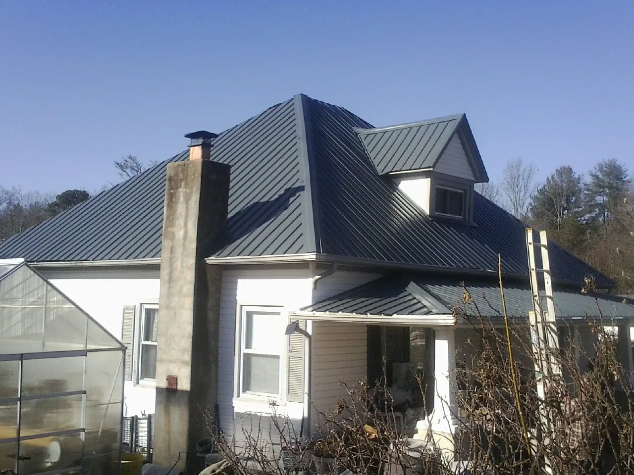 Dark blue standing seam metal roof on a white farmhouse with dormer — Slate & Tile Roof Repair by Roofing Brothers in Simpson