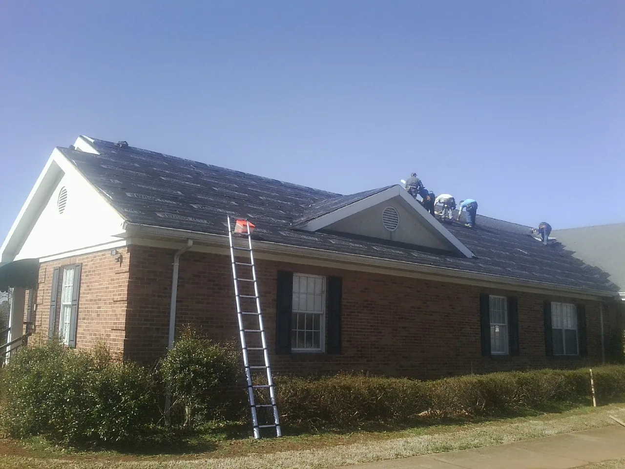 Crew tearing shingles off a brick ranch roof with a ladder set — Emergency Roof Repair work by our crew in Simpson