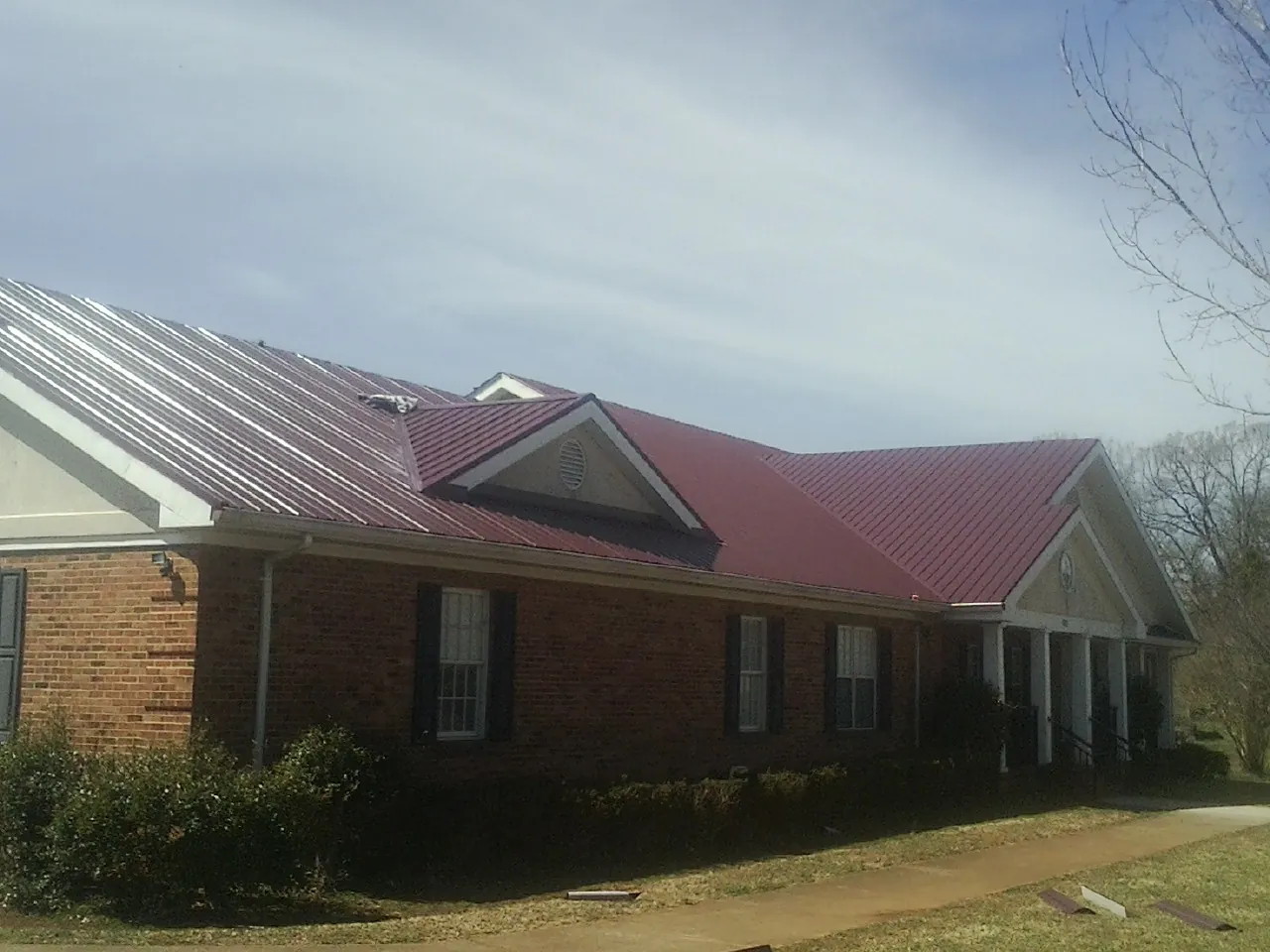 Red metal roof with gabled entries on a long brick building, from a Hail Damage Roof Repair job in Simpson