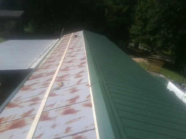 Old rusted panels beside newly installed green metal roofing — Wind Damage Roof Repair by Roofing Brothers in Simpson