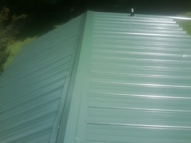 New green metal panels meeting at the ridge of a roof — Flat Roof Repair work by our crew in Simpson