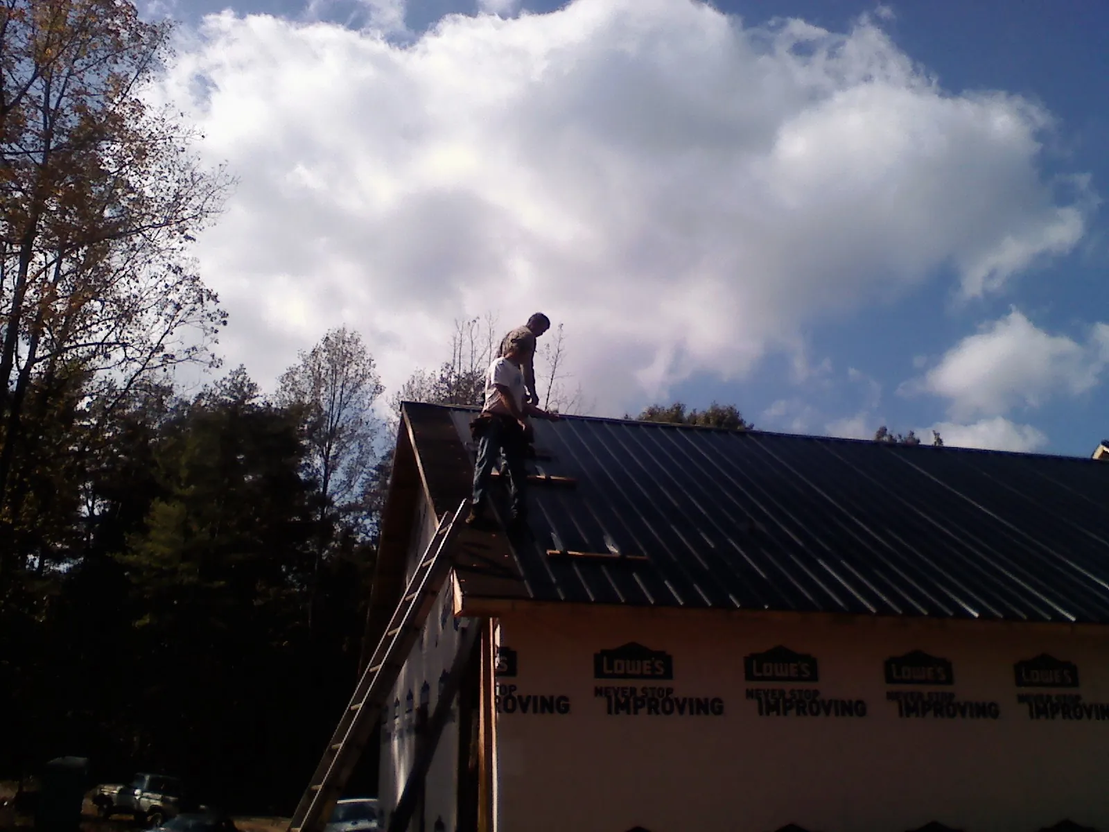 Roofer fastening dark metal panels high against a cloudy sky, from a Roof Inspection job in Simpson